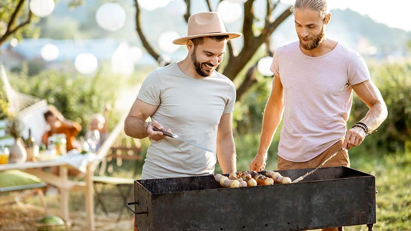 twee mannen staan in de natuur samen te barbecueën op een houtskool bbq